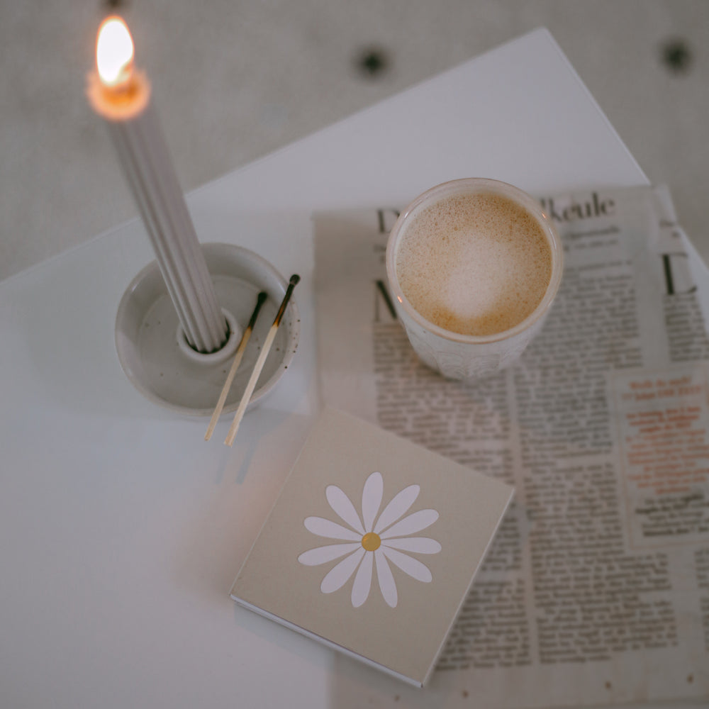 Streichhölzer Daisy neben Kerze und Kaffee auf Zeitung – gemütliche Morgenstimmung mit stilvollem Zubehör.