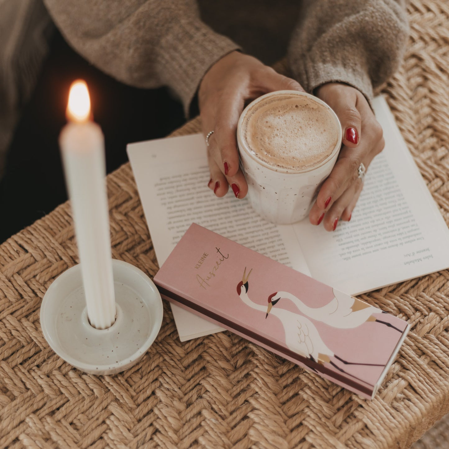 Streichholzschachtel „Kleine Auszeit“ mit Kranich-Motiv neben Kerze und Kaffeetasse