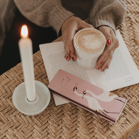 Streichholzschachtel „Kleine Auszeit“ mit Kranich-Motiv neben Kerze und Kaffeetasse