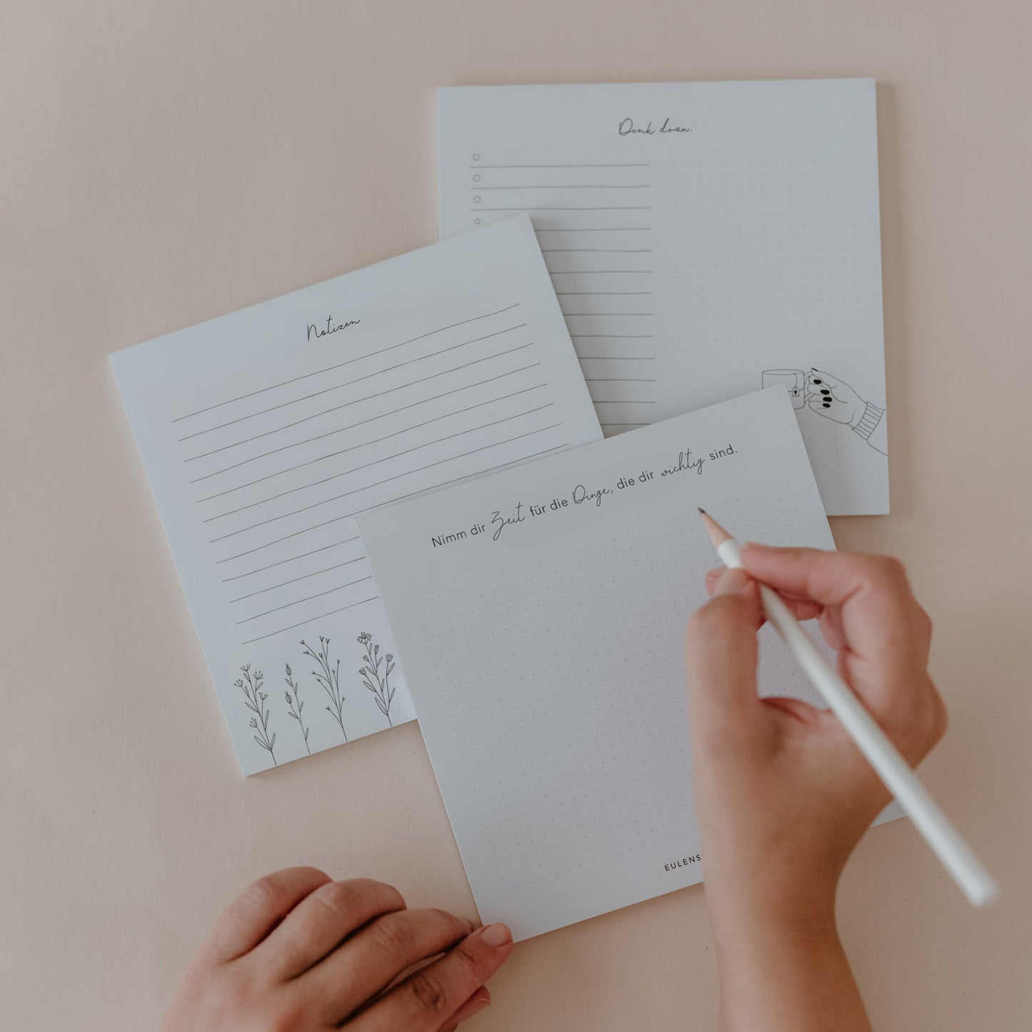 Hand schreibt auf einem Notizblock aus dem 3er Set „Nimm dir Zeit“ mit drei verschiedenen Designs für Listen und Notizen.