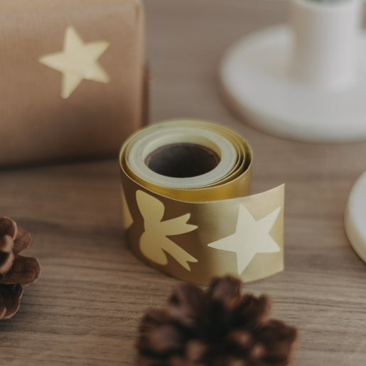 Goldene Stickerrolle mit Motivansicht auf Holzuntergrund, daneben verpacktes Geschenk