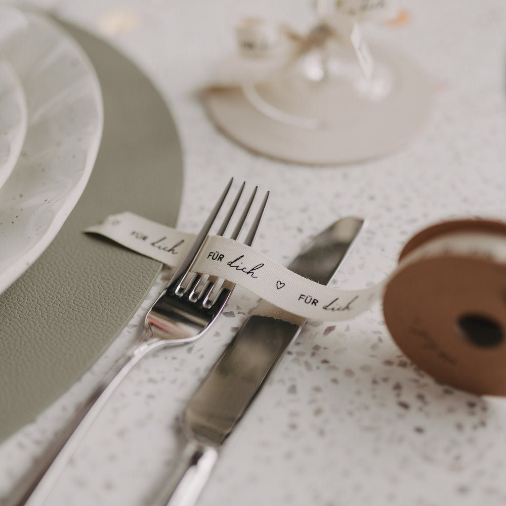 Besteck am gedeckten Tisch mit Geschenkband „Für dich“ gebunden.