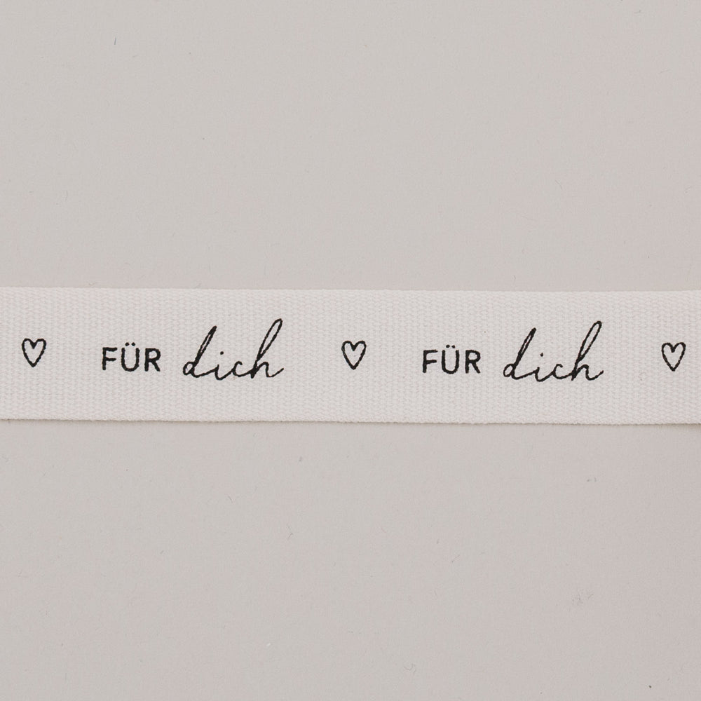 Detailaufnahme vom Geschenkband „Für dich“ mit Herzen, schwarzer Schrift auf weißem Baumwollband.