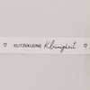 Nahaufnahme des Baumwollbands mit Aufdruck „Klitzekleine Kleinigkeit“ und kleinen Herzsymbolen
