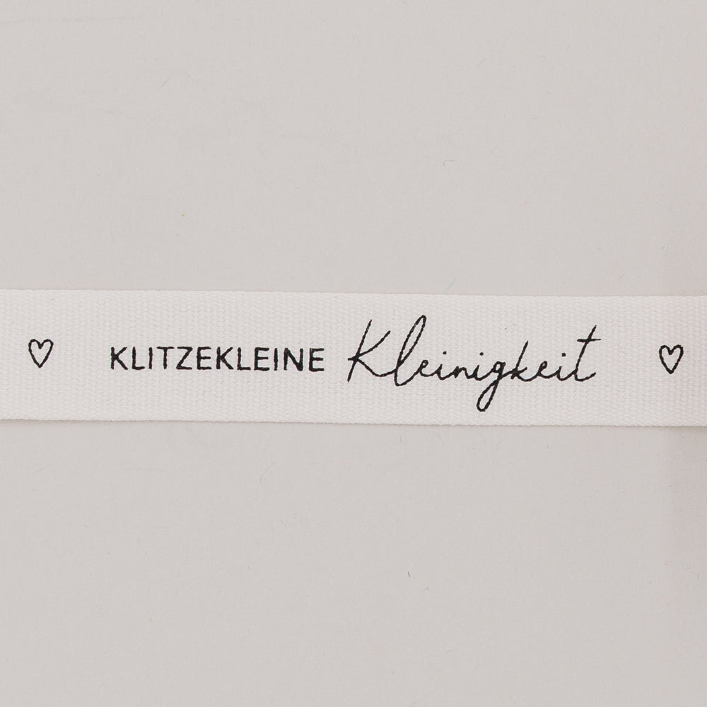 Nahaufnahme des Baumwollbands mit Aufdruck „Klitzekleine Kleinigkeit“ und kleinen Herzsymbolen
