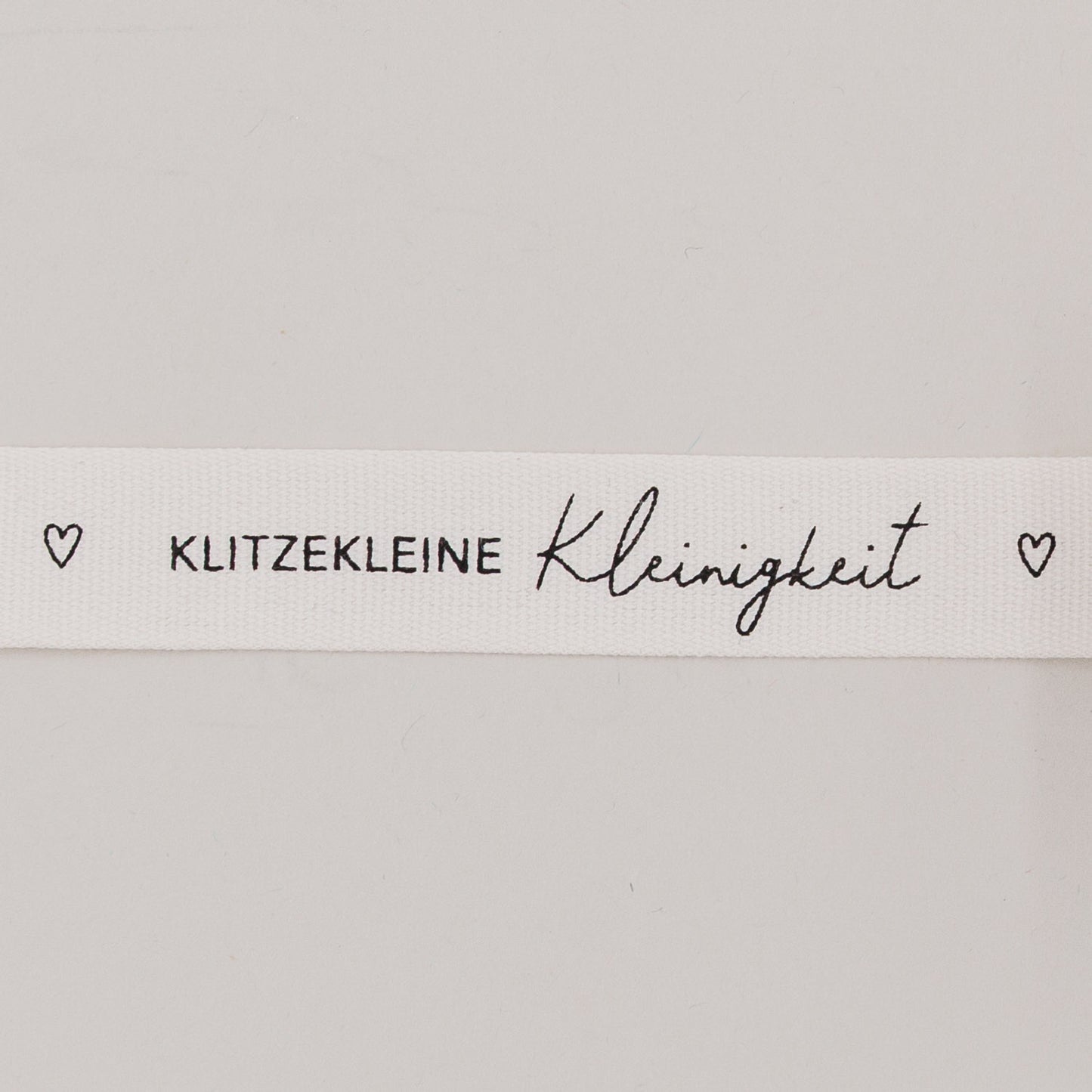 Nahaufnahme des Baumwollbands mit Aufdruck „Klitzekleine Kleinigkeit“ und kleinen Herzsymbolen