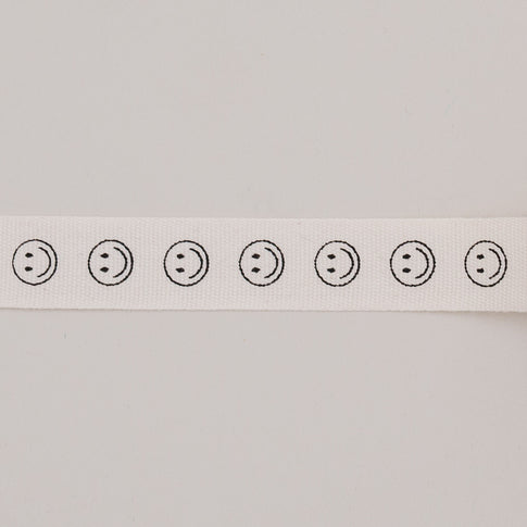 Nahaufnahme des Geschenkbandes Smileys, zeigt schwarze Smileymotive in Reihe auf naturweißem Baumwollband