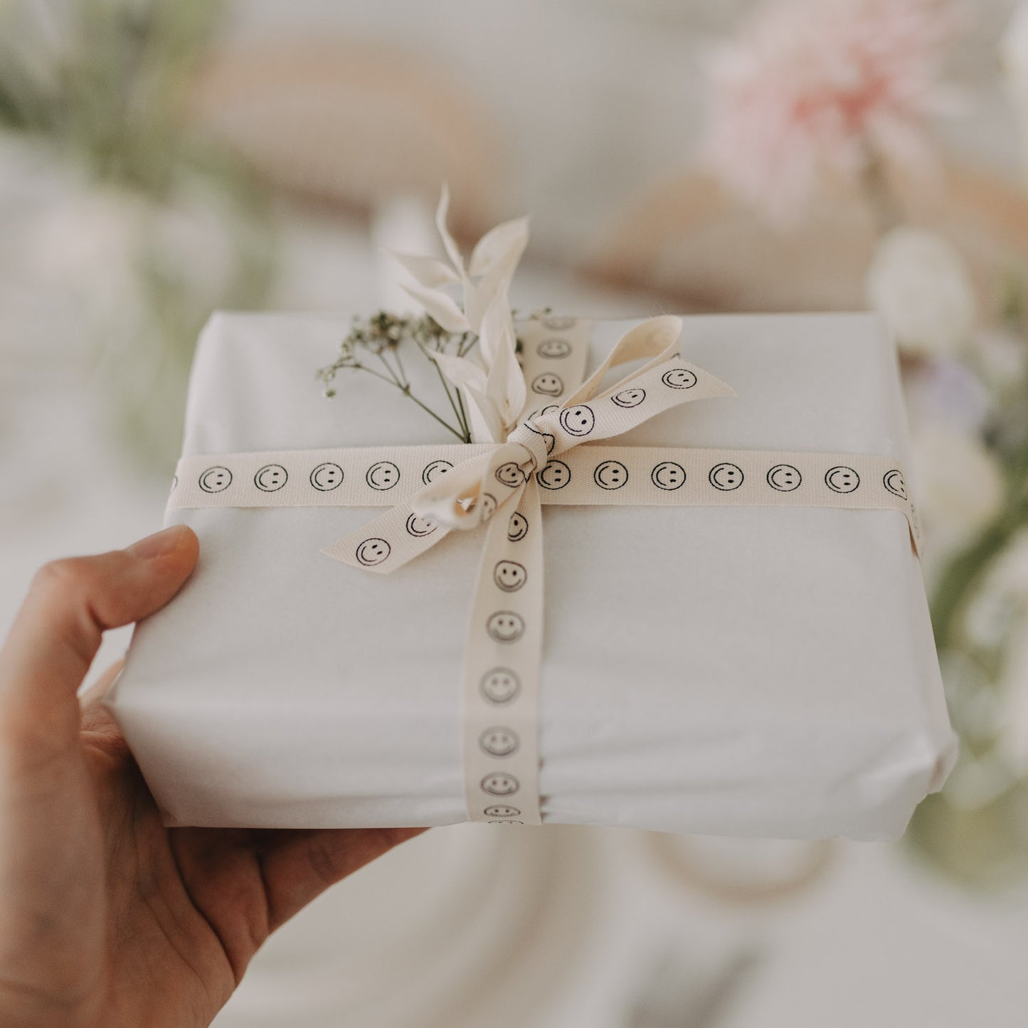 Geschenk mit weißem Papier und Smiley-Geschenkband, dekoriert mit Trockenblumen.