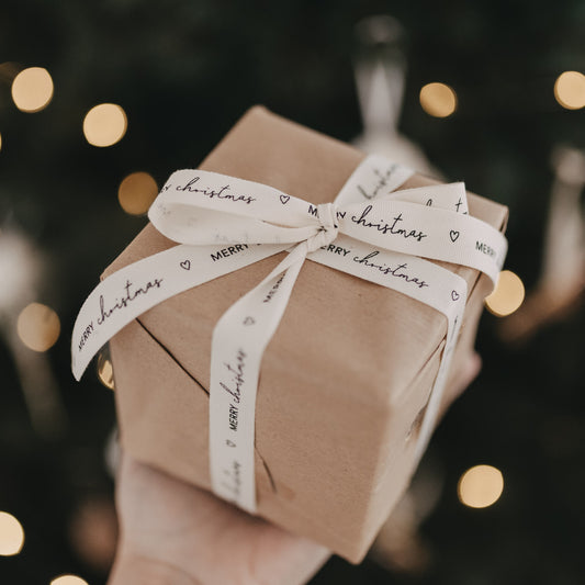 Geschenk mit Baumwollband Merry Christmas liebevoll verpackt vor Weihnachtsbaumlichtern