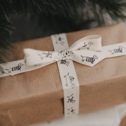 Geschenkband mit Dackelmotiv auf Geschenk, verpackt in braunem Papier, Schleife unter Tannenzweigen