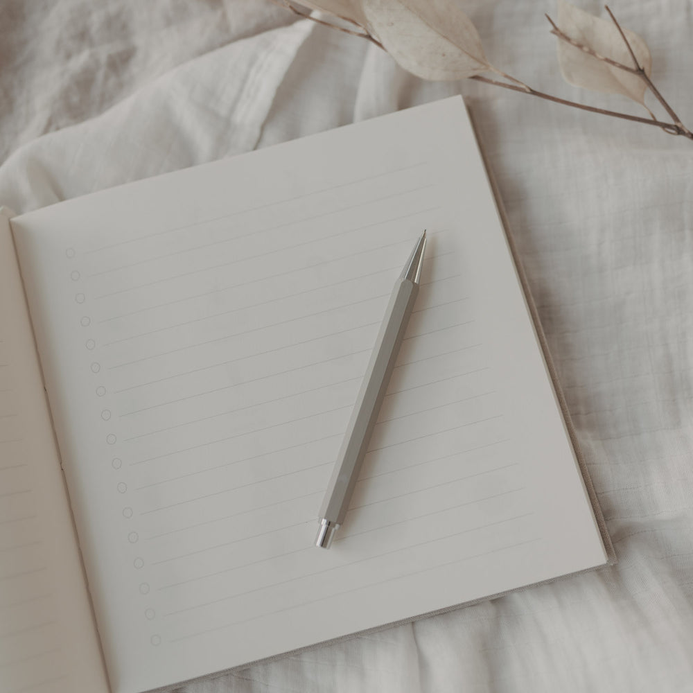 Grauer Druckbleistift auf linierten Notizbuchseiten, stilvoll präsentiert auf weißem Stoff.