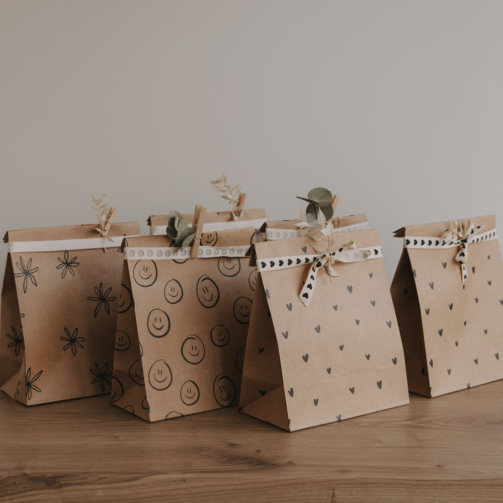 Papier Geschenktüten mit Herz-, Smiley- und Blumenmotiven im Set, dekorativ aufgereiht auf Holztisch