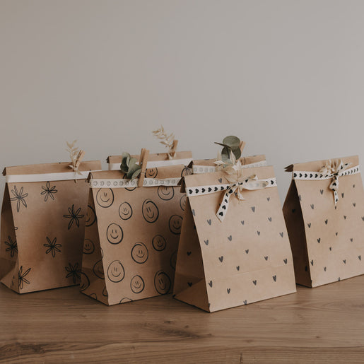 Papier Geschenktüten mit Herz-, Smiley- und Blumenmotiven im Set, dekorativ aufgereiht auf Holztisch