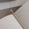 Weißer Bleistift mit Herzdetail auf aufgeschlagenem Wochenplaner