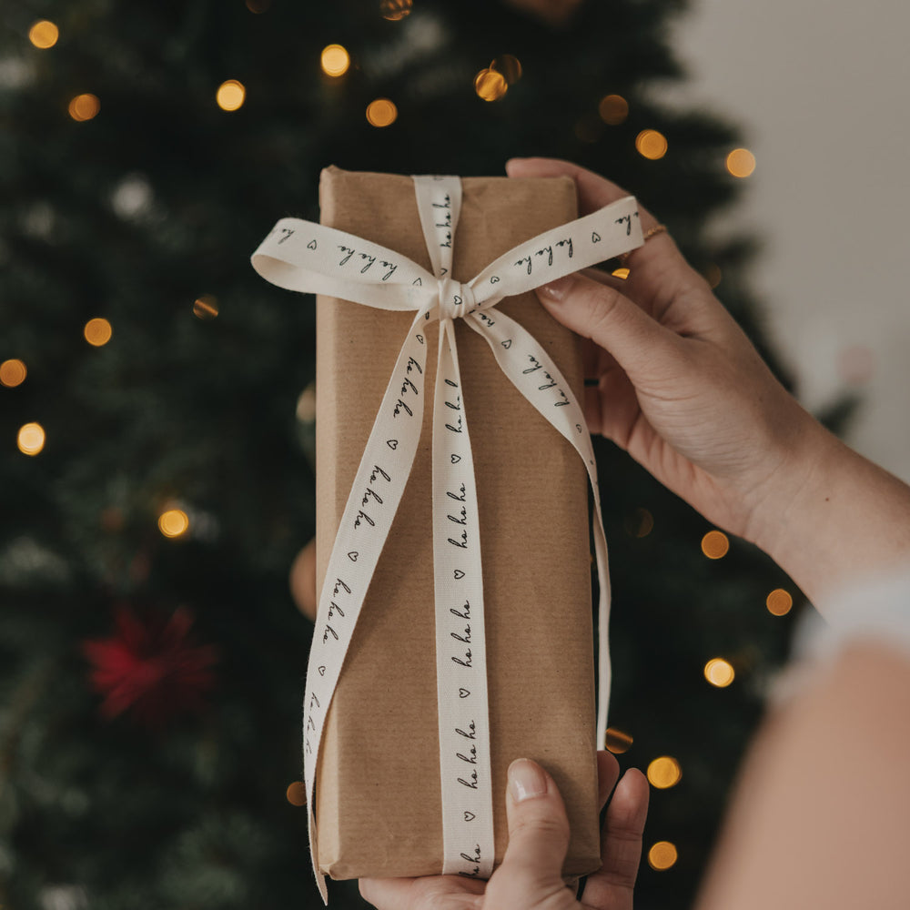 Weihnachtsgeschenk mit Eulenschnitt Geschenkband Ho Ho Ho vor beleuchtetem Weihnachtsbaum