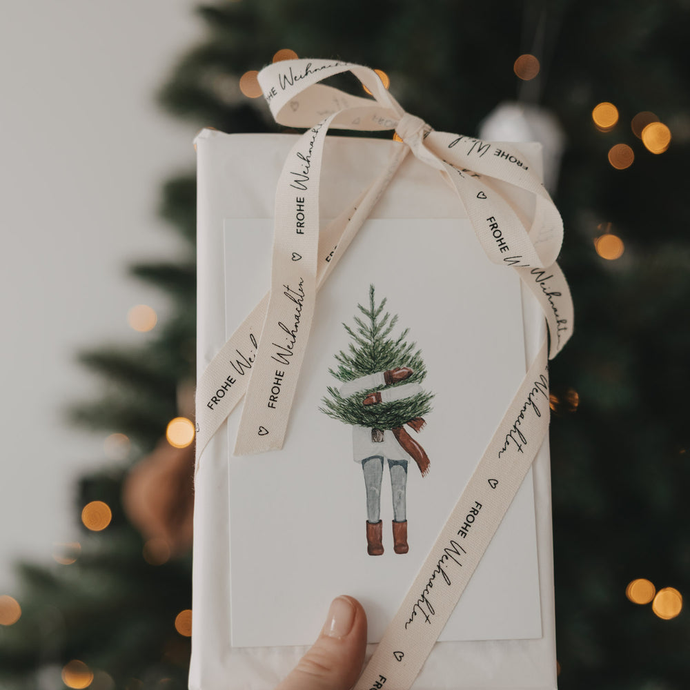 Weihnachtsgeschenk mit Eulenschnitt Geschenkband Frohe Weihnachten vor beleuchtetem Weihnachtsbaum