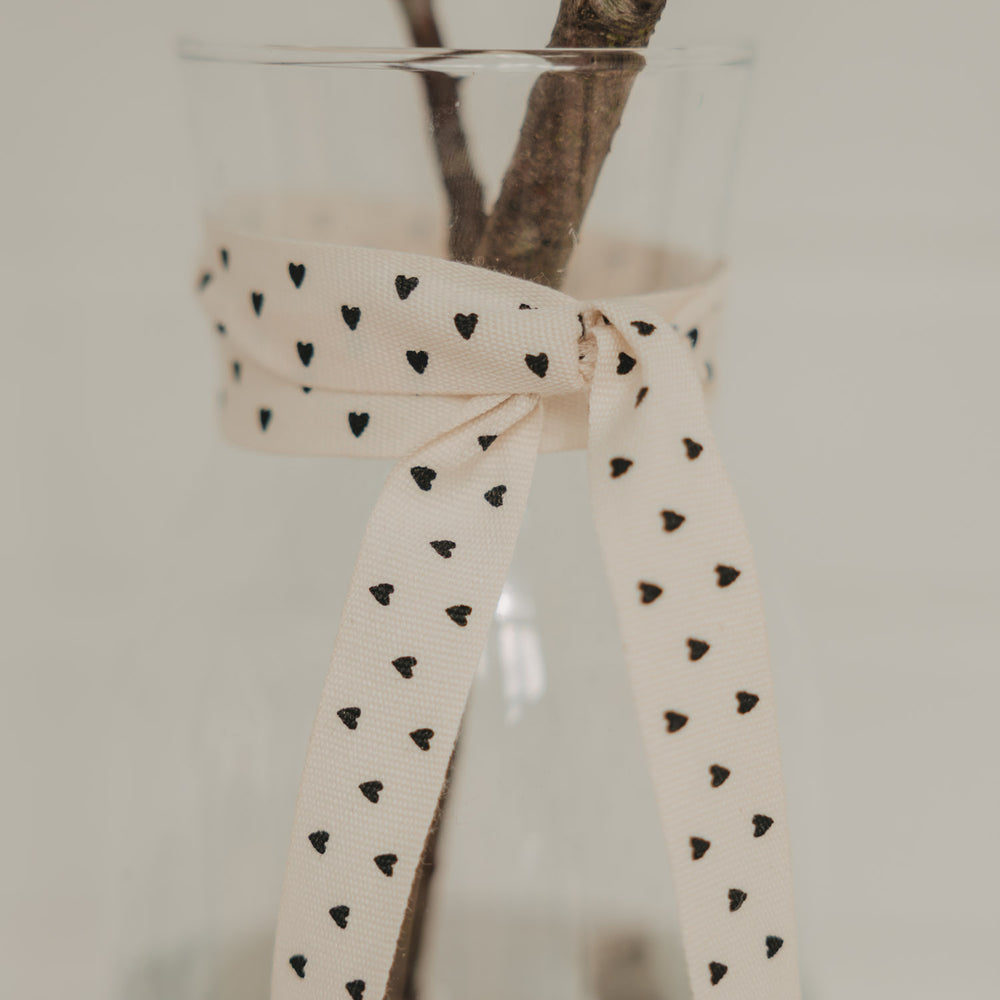Beiges Geschenkband mit schwarzen Herzen als Schleife an einer Glasvase