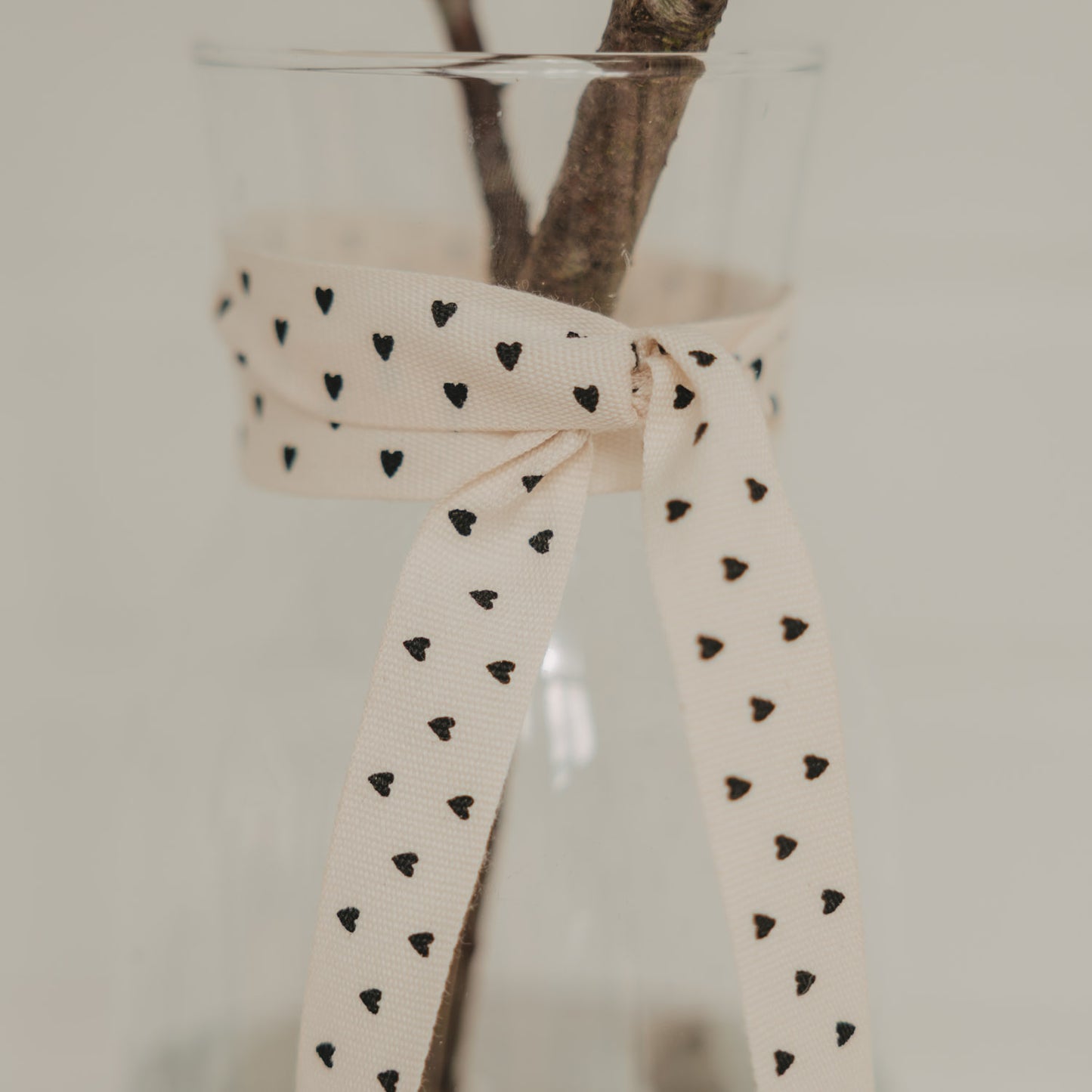 Beiges Geschenkband mit schwarzen Herzen als Schleife an einer Glasvase