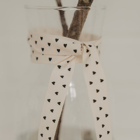 Beiges Geschenkband mit schwarzen Herzen als Schleife an einer Glasvase
