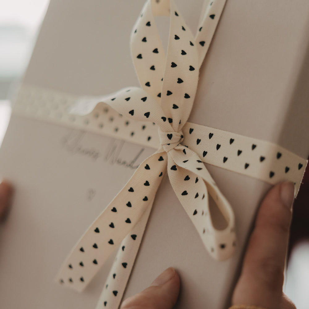 Detailansicht einer Schleife aus beigem Geschenkband mit schwarzen Herzen