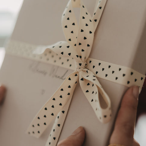 Detailansicht einer Schleife aus beigem Geschenkband mit schwarzen Herzen