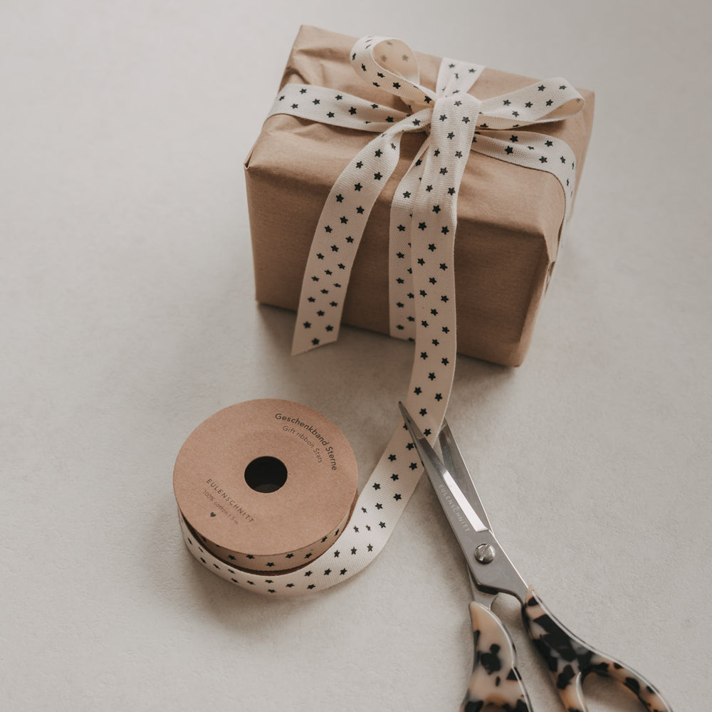 Beiges Geschenkband mit schwarzen Sternen, Geschenk, Rolle und Schere