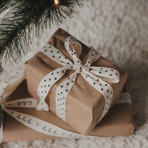 Geschenk mit beigem Geschenkband und schwarzen Sternen unter einem Weihnachtsbaum