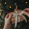 Geschenk mit beigem Geschenkband und schwarzen Sternen vor einem Weihnachtsbaum