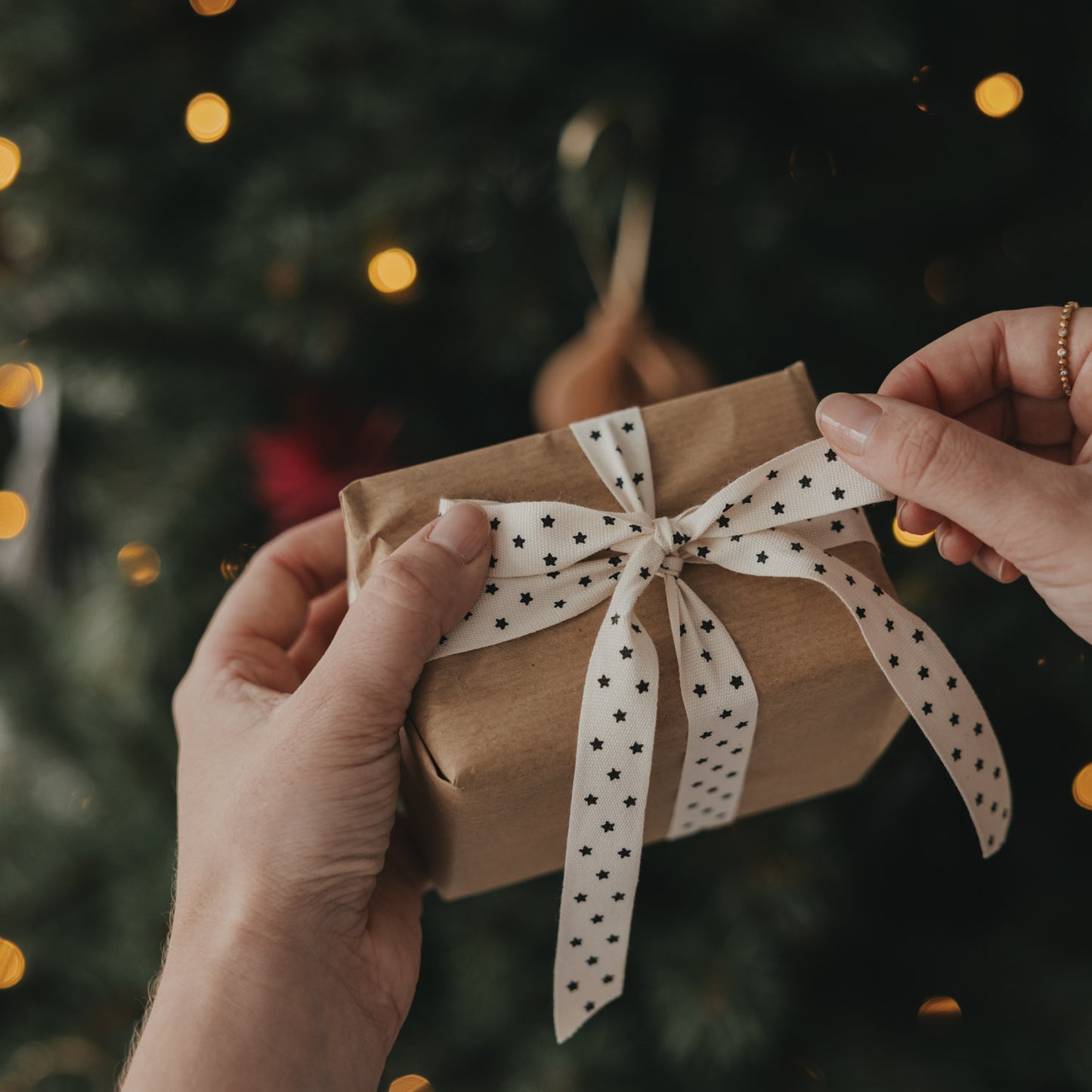 Geschenk mit beigem Geschenkband und schwarzen Sternen vor einem Weihnachtsbaum