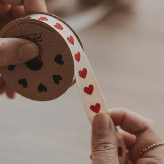 Beiges Geschenkband mit roten Herzen auf Rolle, in den Händen gehalten