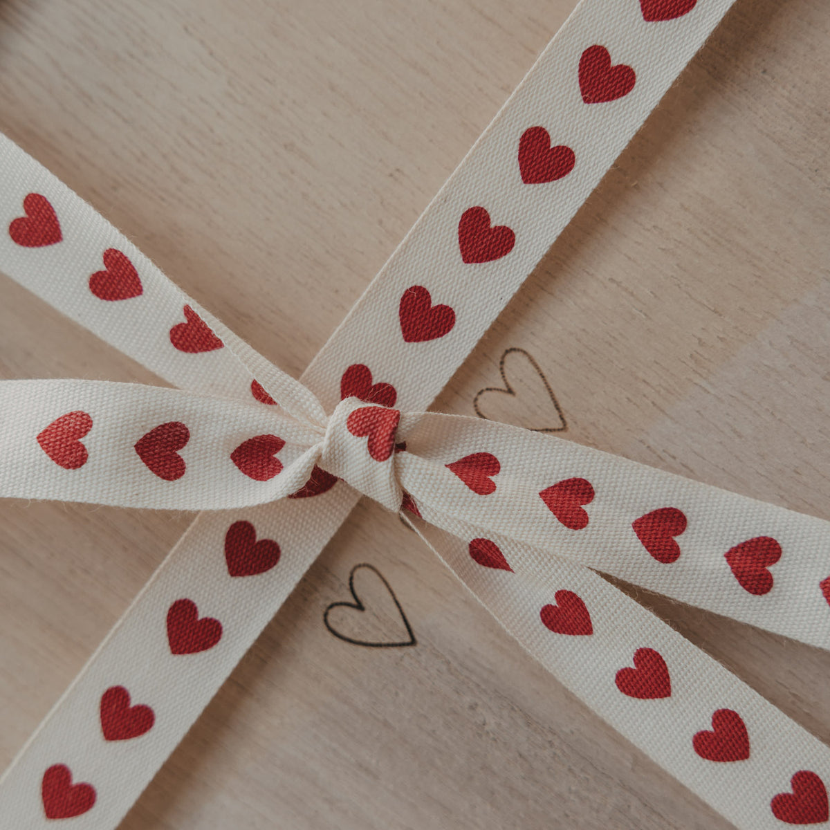 Geschenkband mit roten Herzen als Schleife auf einer hellen Holzbox
