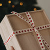 Holzbox mit beigem Geschenkband und roten Herzen vor einem Weihnachtsbaum