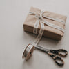 Beiges Geschenkband mit Nussknacker-Motiv neben Schere und weihnachtlich verpacktem Geschenk