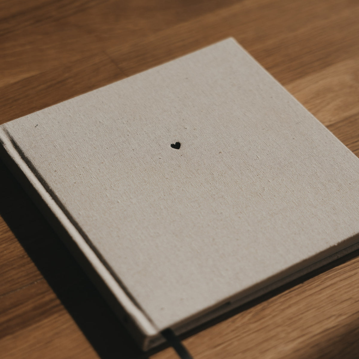 Quadratisches Buch mit beigem Leineneinband, schwarzem Herz und schwarzem Leseband