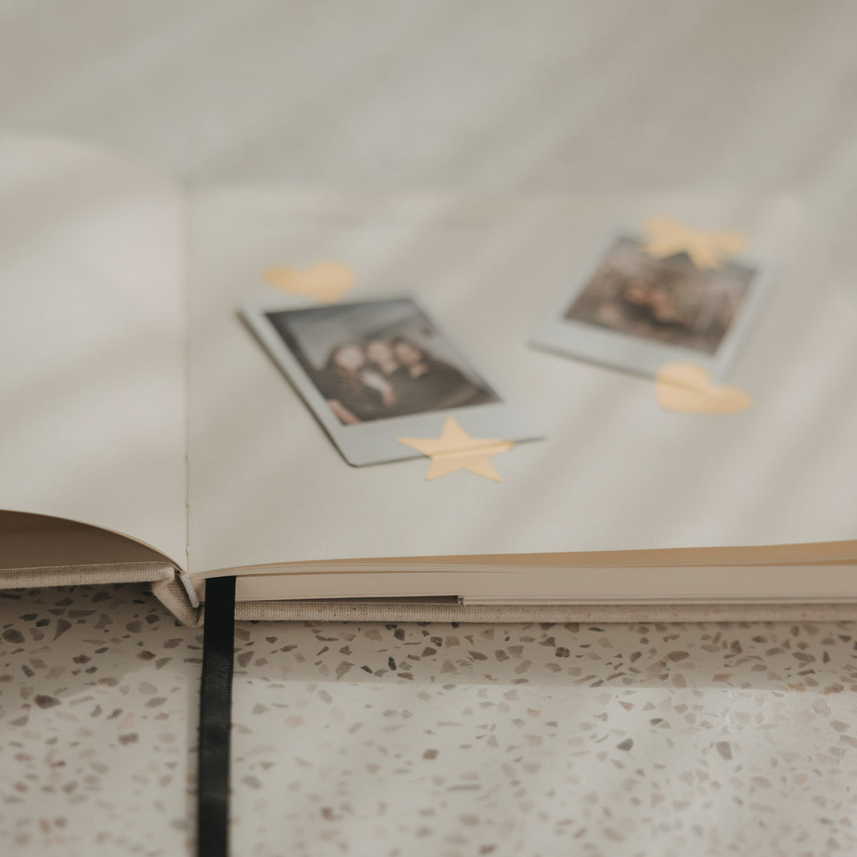 Detailansicht eines offenen Buchs mit Blankoseiten, Fotos und goldenen Stickern