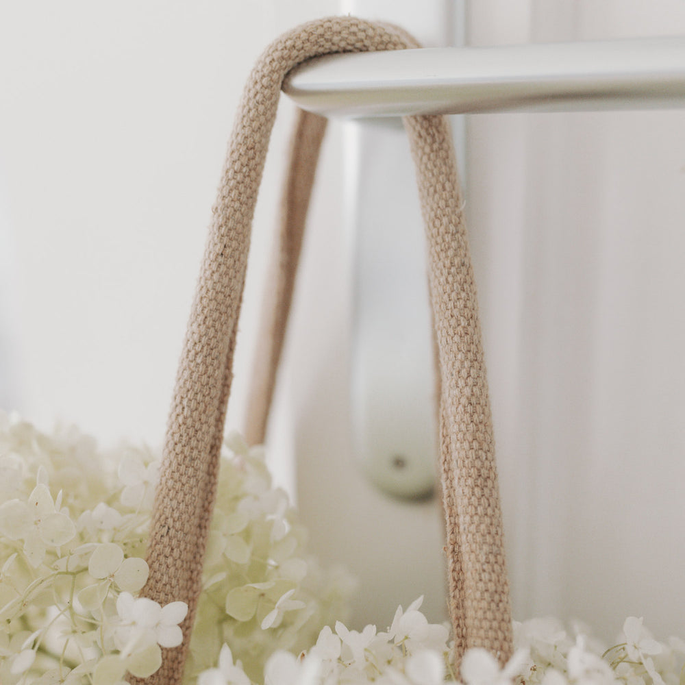 Detailaufnahme des Henkels der Tasche, daneben weiße Blüten – Fokus auf Verarbeitung und Material.