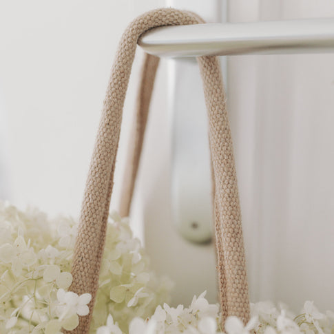 Detailaufnahme des Henkels der Tasche, daneben weiße Blüten – Fokus auf Verarbeitung und Material.