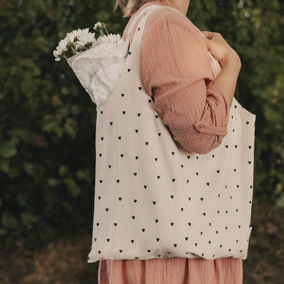 Große faltbare Baumwolltasche mit schwarzen Herzen über der Schulter getragen und mit Blumen gefüllt