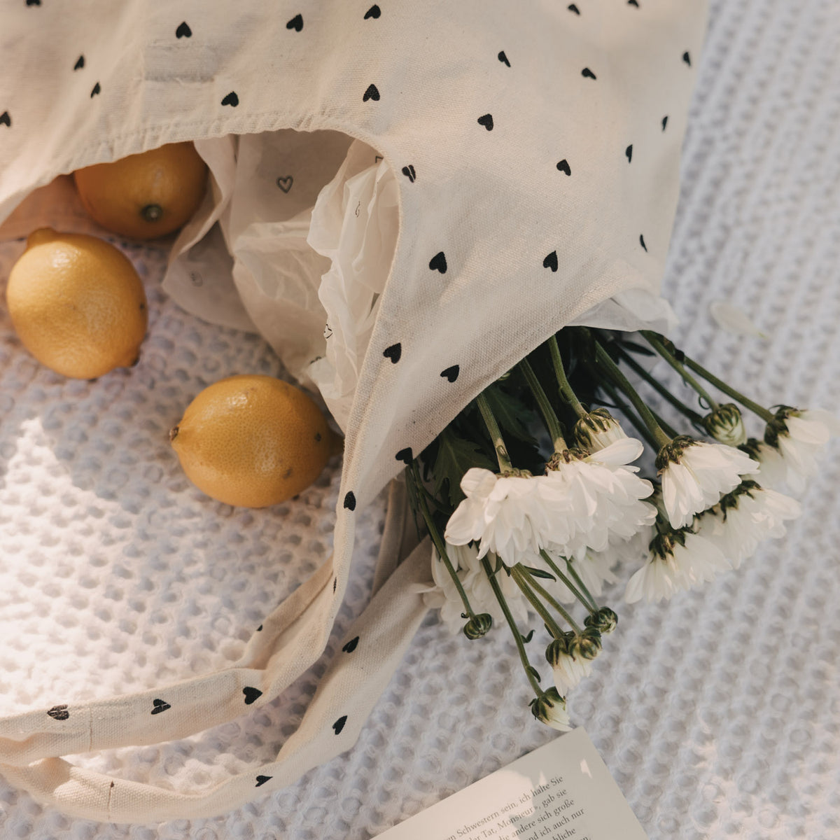 Baumwolltasche mit schwarzen Herzen, gefüllt mit weißen Blumen und Zitronen