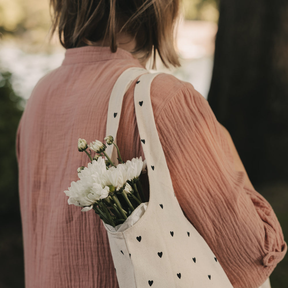 Baumwolltasche mit schwarzen Herzen über der Schulter getragen und mit weißen Blumen gefüllt