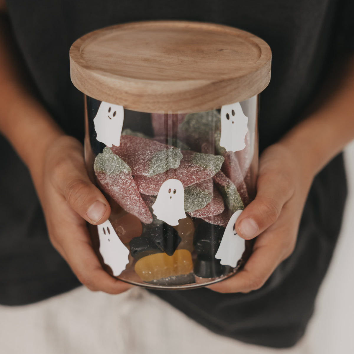 Vorratsglas mit weißen Geistermotiven und Holzdeckel, gefüllt mit bunten Süßigkeiten