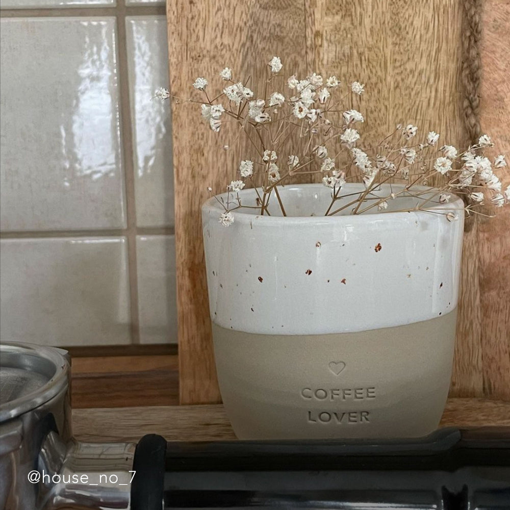 Auf einer Küchenzeile steht ein Becher mit der Prägung "Coffee Lover" und Schleierkraut guckt aus ihm heraus.