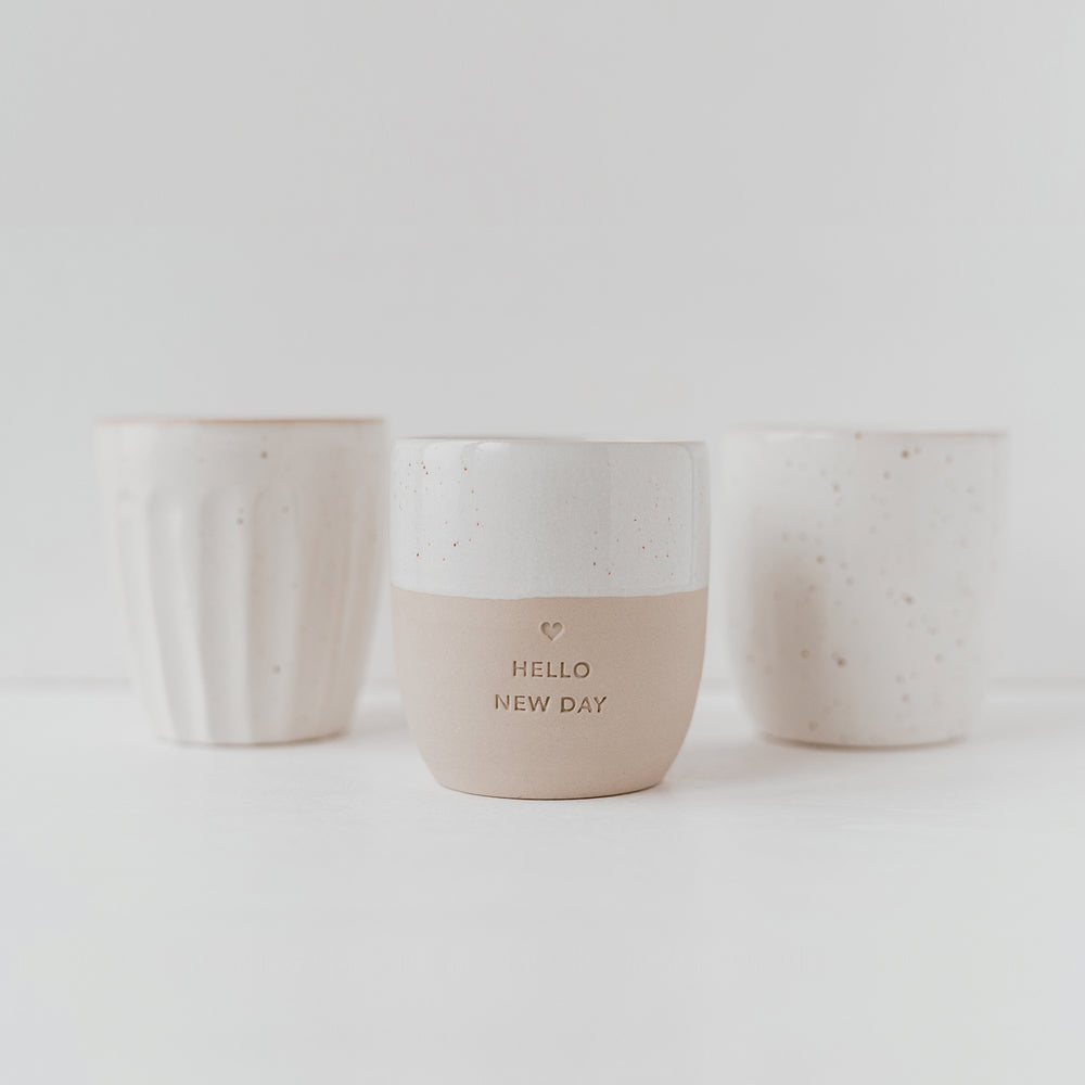 Im Vordergrund steht ein Becher mit der Prägung "Hello New Day" dahinter 2 Becher ohne Prägung.