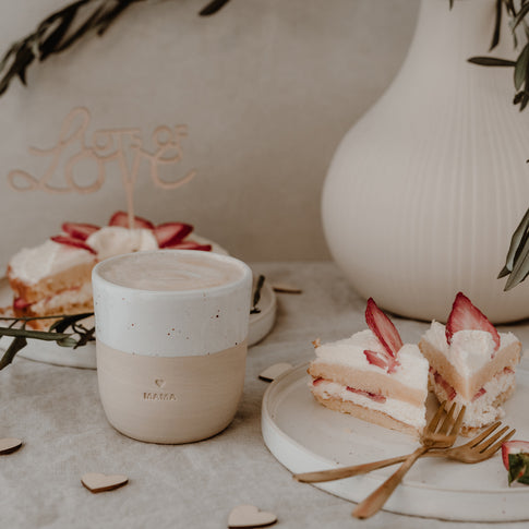 Gedeckter Tisch mit Erdbeerkuchen und Tellern und Gabel. Im Fokus ein Becher mit der Prägung "Mama".
