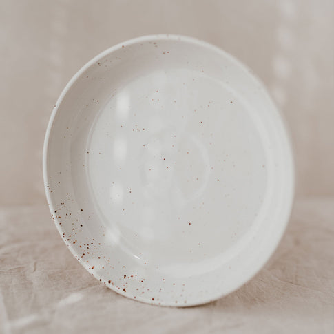 Der tiefe Teller ist frontal von oben aufgenommen und zeigt die gesprenkelte, glänzend glasierte Oberfläche auf hellem Stoff.