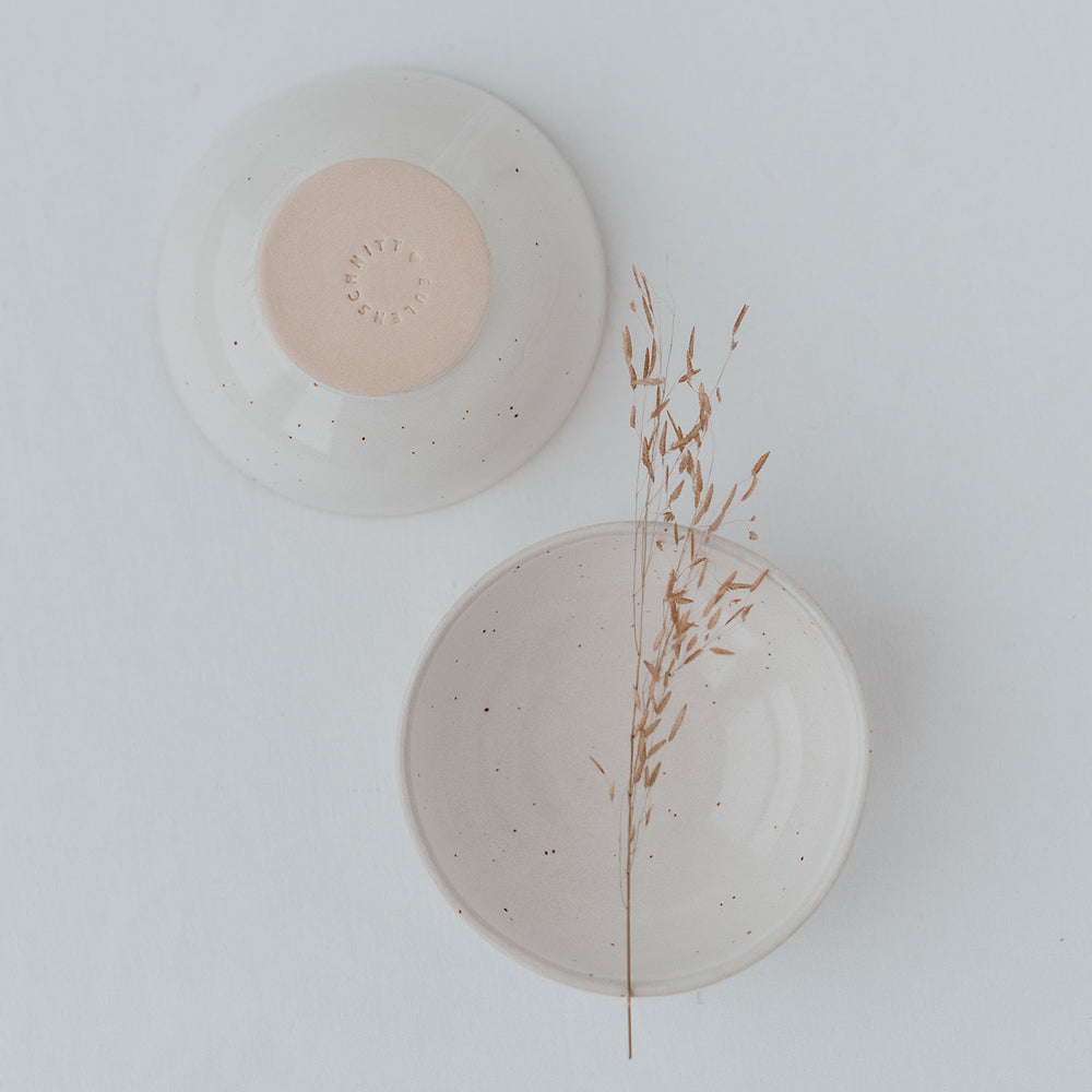 Zwei Keramikschalen von oben fotografiert: eine mit der Unterseite nach oben, die andere geöffnet mit einem zarten Grashalm darin. Die Unterseite ist naturfarben mit eingeprägtem Schriftzug „Eulenschnitt“.