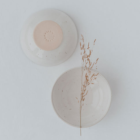 Zwei Keramikschalen von oben fotografiert: eine mit der Unterseite nach oben, die andere geöffnet mit einem zarten Grashalm darin. Die Unterseite ist naturfarben mit eingeprägtem Schriftzug „Eulenschnitt“.