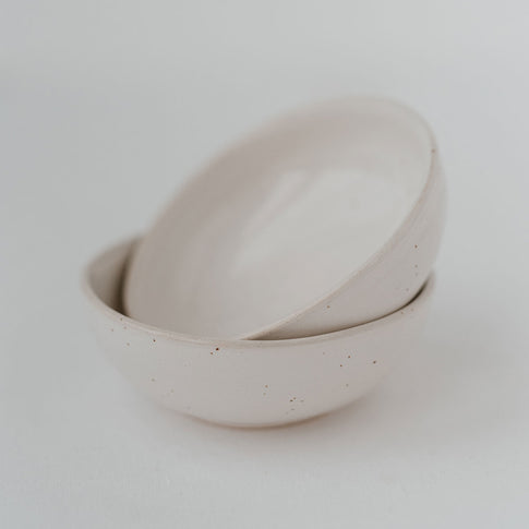 Zwei matte Keramikschalen in Beige mit brauner Sprenkelung, leicht versetzt ineinandergelegt. Die Aufnahme ist hell und minimalistisch vor weißem Hintergrund gestaltet.