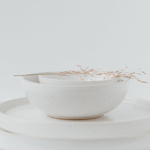 Zwei übereinandergelegte Schalen aus gesprenkelter Keramik auf 2 weißen Keramiktellern.